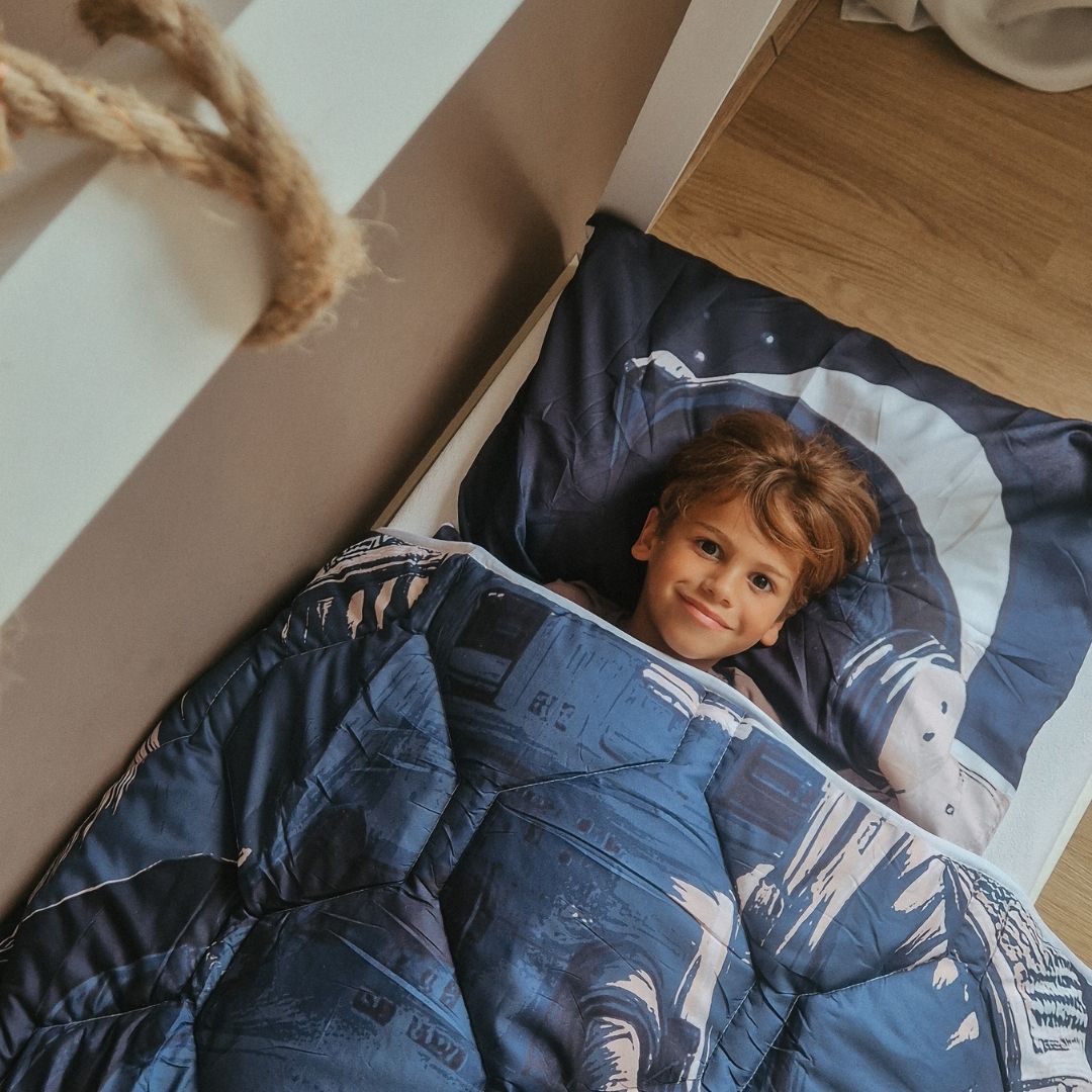 Child lying under Thehappybed Astronaut kids duvet with matching pillowcase featuring astronaut print